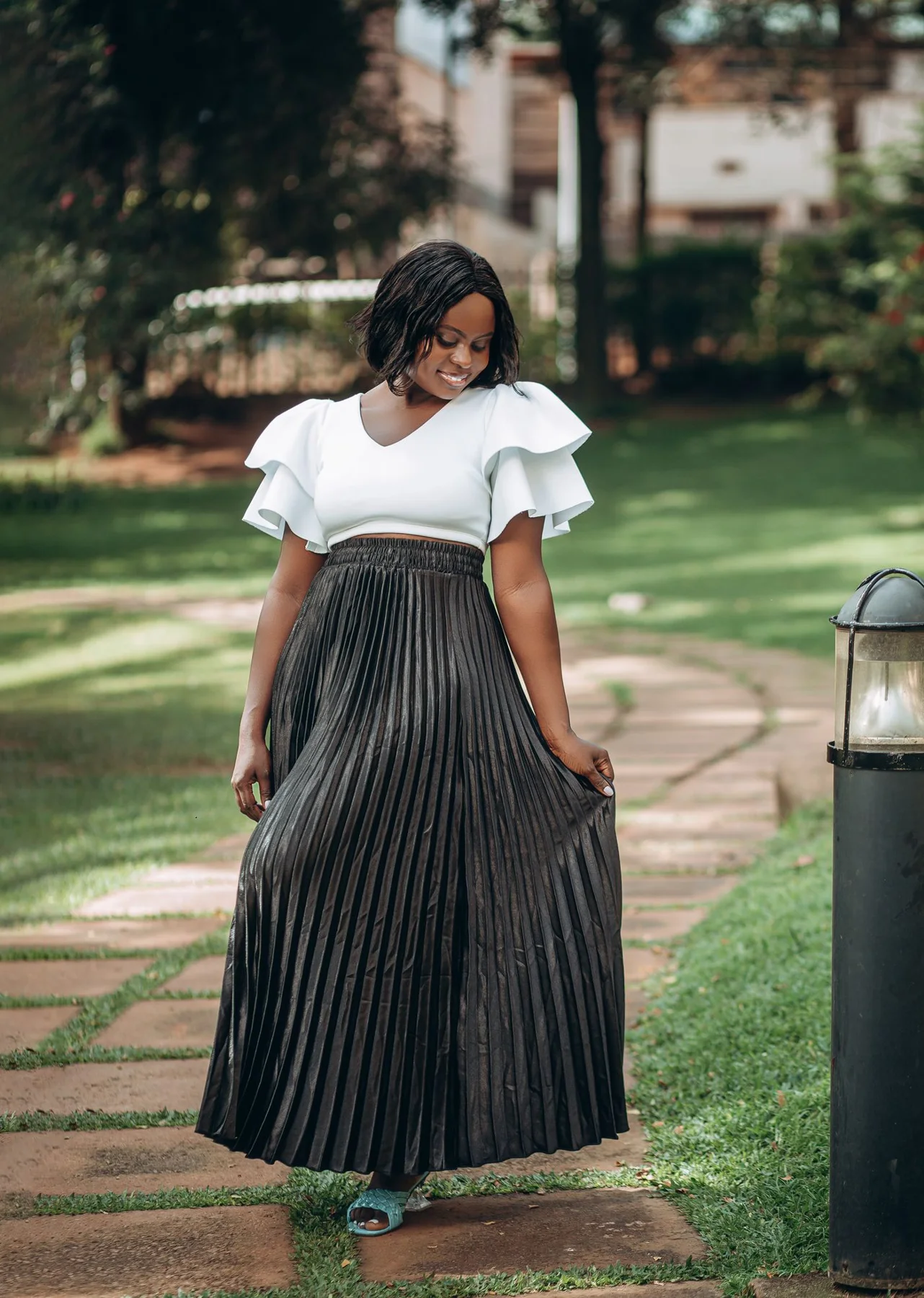 A woman wearing a long pleated skirt and white top on a park path.