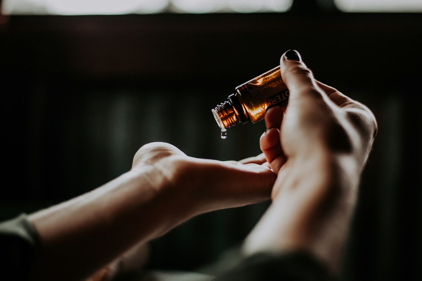 Hands holding an open amber bottle above a palm