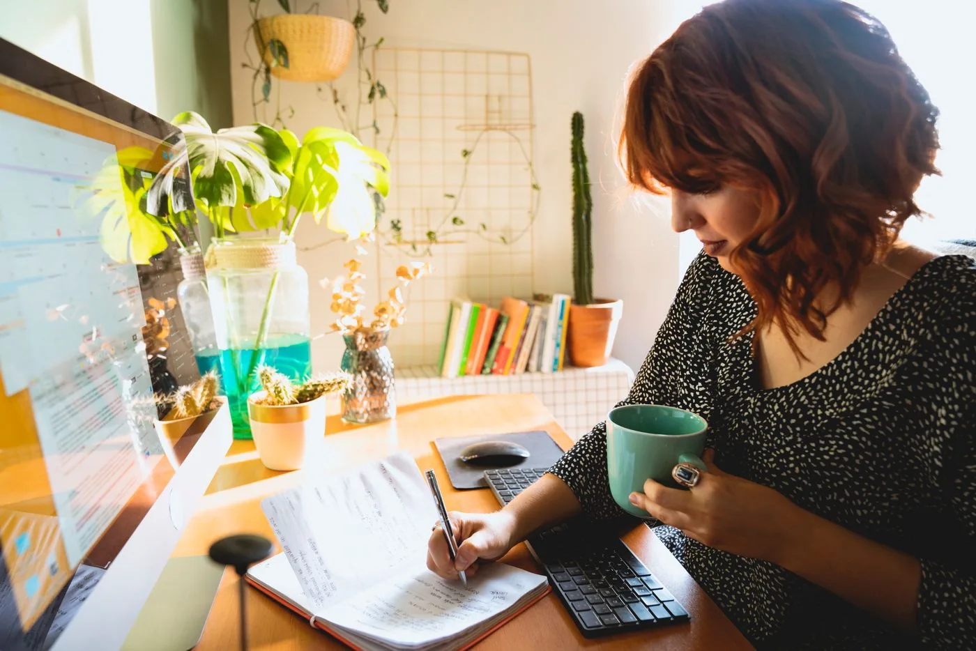Woman writing on paper while holding a green mug at a desk