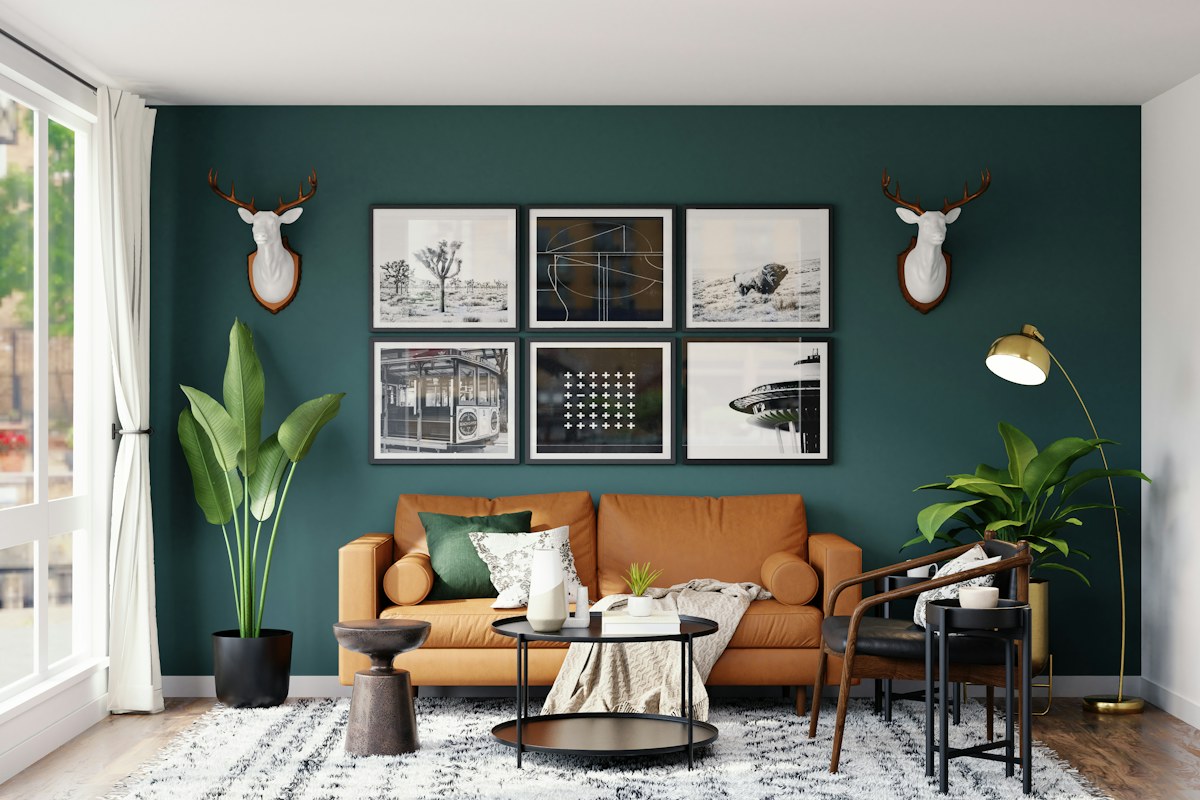 Tan sofa against a dark green wall beneath a group of framed prints