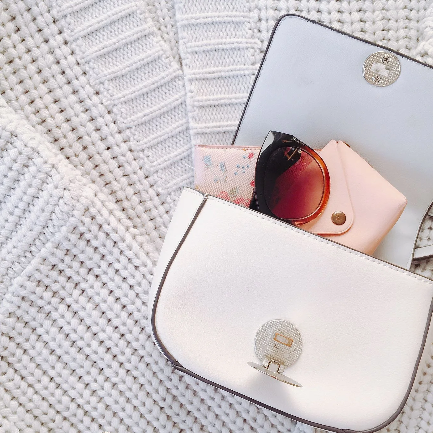 White structured bag and sunglasses arranged on pale knitwear