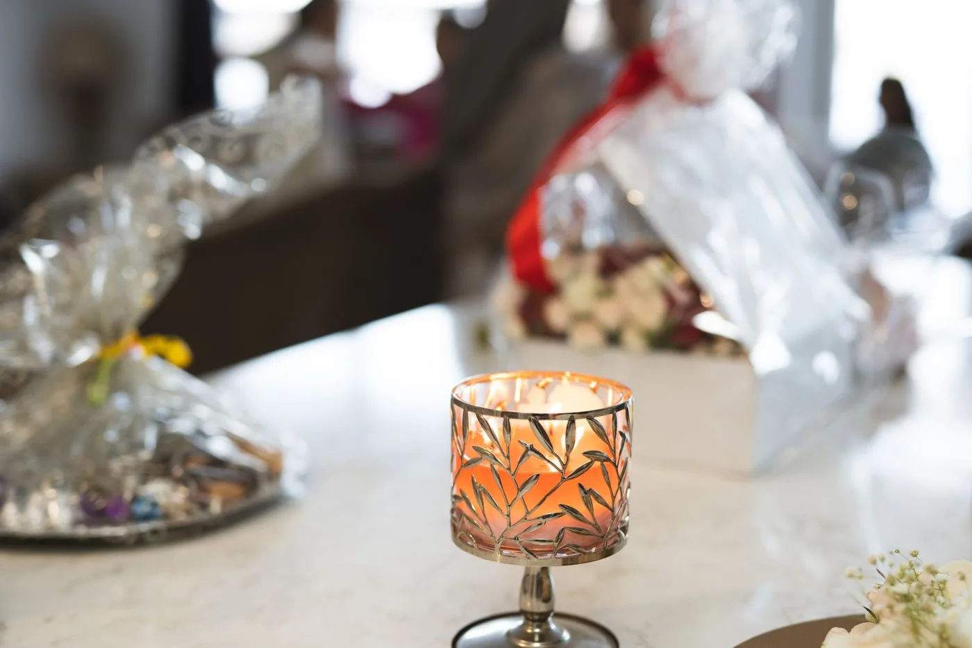 A lit patterned candle holder with a wrapped object in the background