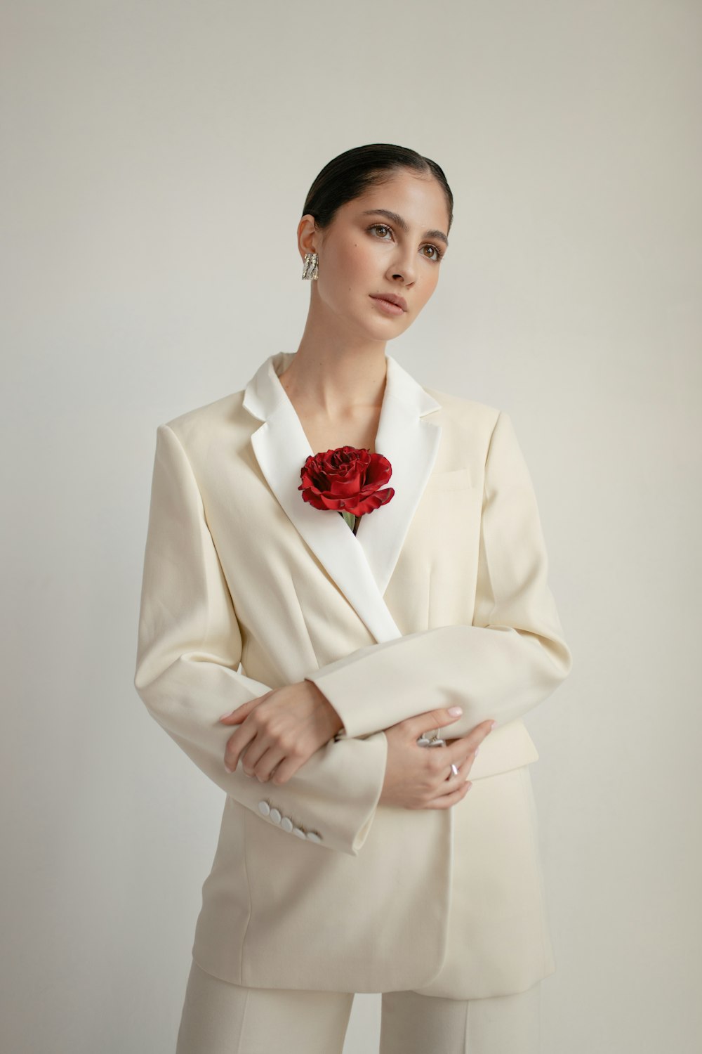 Woman wearing a pale jacket with a red floral accent near its lapel