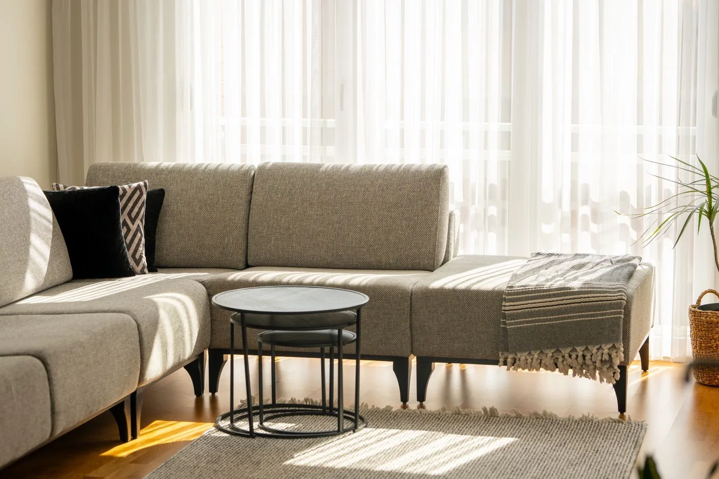 A pale sectional sofa and small tables beside tall windows with curtains