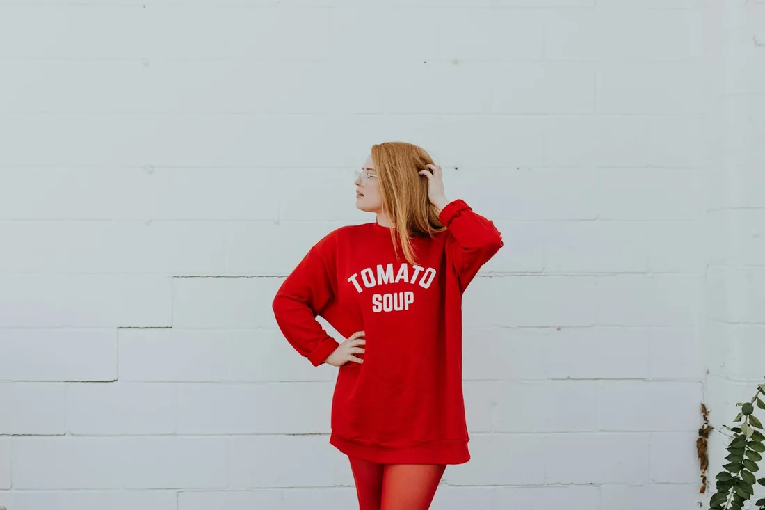 Woman wearing a red oversized sweatshirt beside a wall