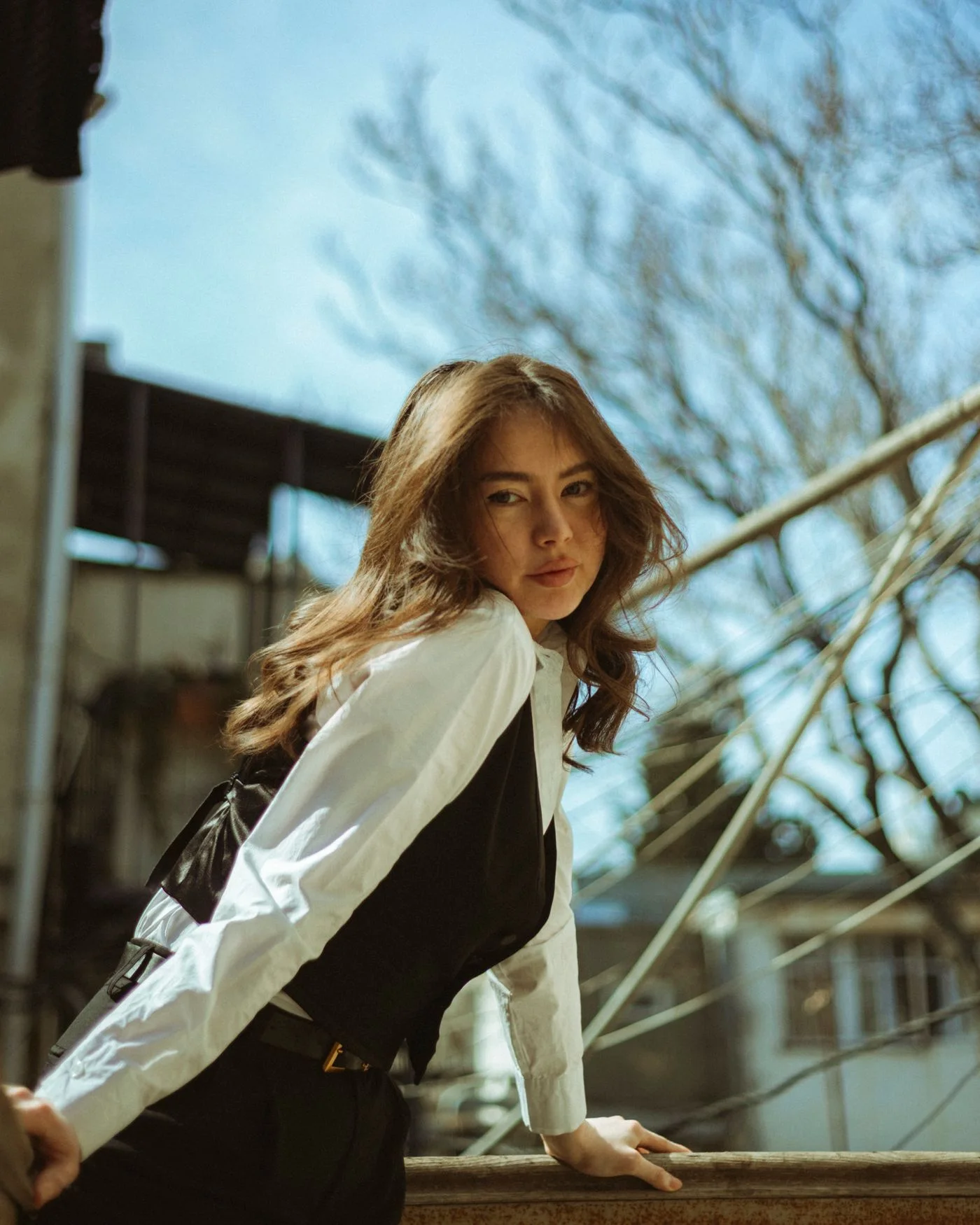A woman wearing a blouse, waistcoat and trousers outdoors.