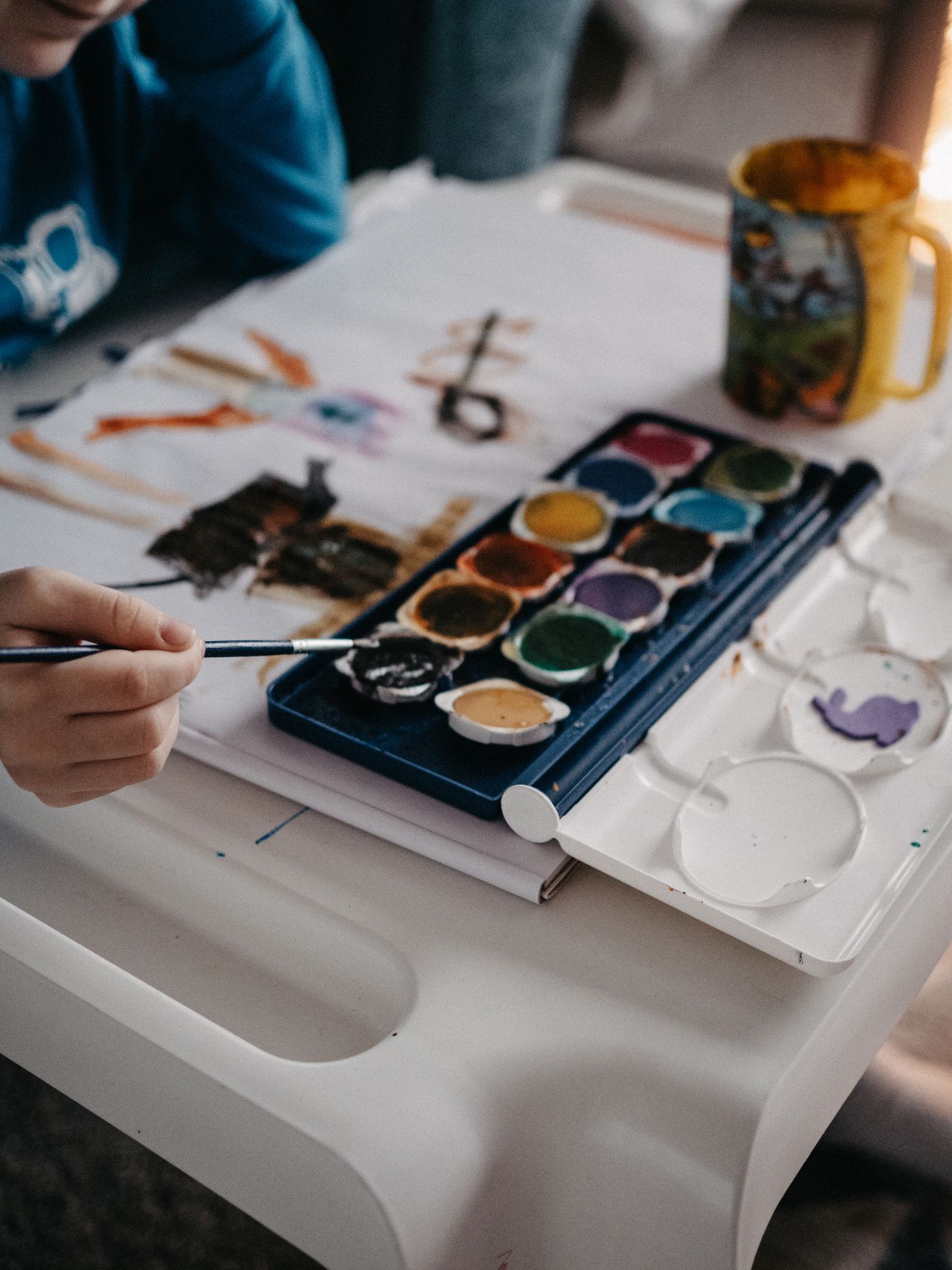 Hands using a brush beside a watercolour paint palette